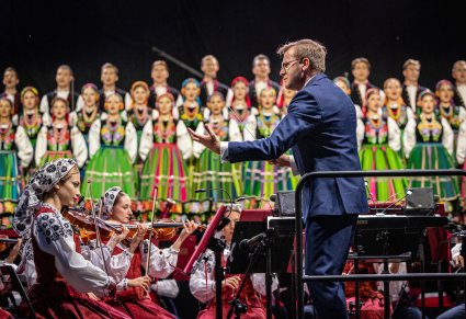 Zbliżenie na dyrygenta, obok część orkiestry w kostiumach wilanowskichw tle chór w kostiumach łowickich,