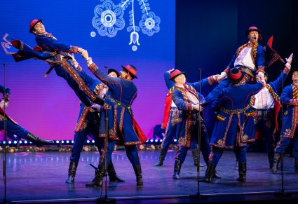 Na scenie grupa Artystów w kostiumach podegrodzkich w trakcie wykonywania choreografii tanecznej