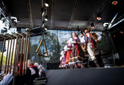 Na pierwszym planie instrumenty perkusyjne takie jak np. trójkąt  na drugim planie Artyści w kostiumach limanowskich