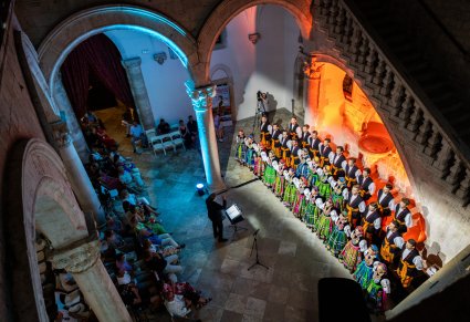 Widok z góry na chór ustawiony w rzędach w kostiumach łowickich a przed nim publiczność