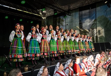 Artyści chóru w kostiumach łowickich na scenie podczas śpiewu a na dole orkiestra