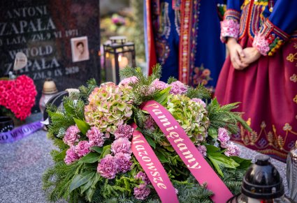 Zbliżenie na wiązankę z napisem "Pamiętamy Mazowsze" na grobie Witolda Zapały, w tle kostiumy podegrodzkie