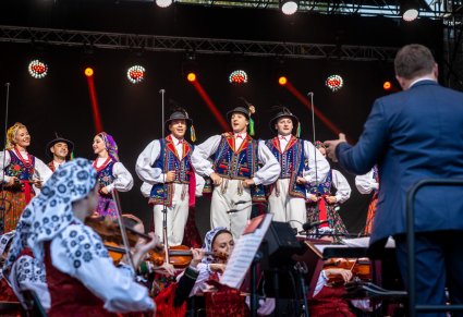 Artyści na scenie w kostiumach limanowskich widoczna orkiestra z Dyrygentem