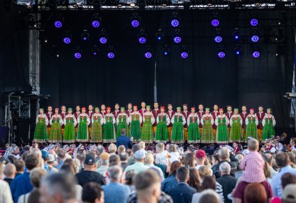 Widok z perspektywy publiczności, na chór w kostiumach kurpiowskich oraz dyrygenta