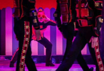 Zbliżenie na Artystkę grającą postać kwadratu w charakterystycznym kostiumie i czerwonym wplatanym warkoczu.