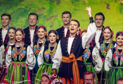 Solista w kostiumie łowickim w trakcie wykonywania pieśni Belgii a za nim reszta Artystów również w kostiumach łowickich