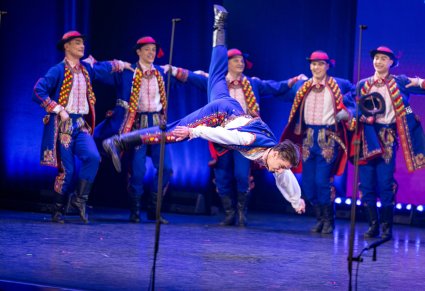 Na pierwszym planie Artysta Baletu w kostiumie podegrodzkim w trakcie wykonywania spektakularnej choreografii tanecznej, w tle reszta Artystów Baletu