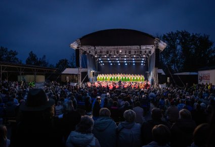 Widok zza publiczności na scenę z chórem w kostiumach kurpiowskich oraz orkiestrą w kostiumach wilanowskich i podhalańskich
