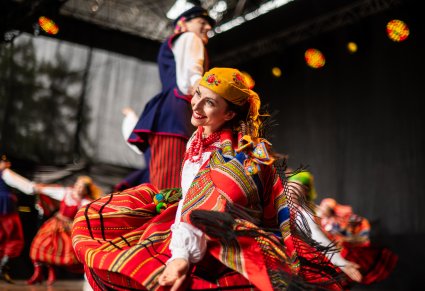 Uśmiechnięta para Artystów w kostiumach sieradzkich na scenie w trakcie wykonywania choreografii tanecznej