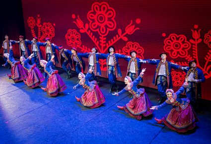 Grupa Artystów w kostiumach podegrodzkich w trakcie wykonywania choreografii tanecznej na scenie