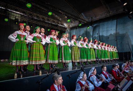 Chór na scenie w rzędzie w kostiumach kurpiowskich a na dole część orkiestry