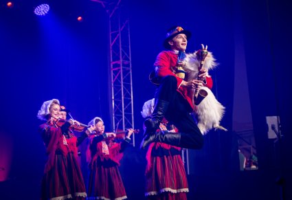 Artysta w kostiumie lubuskim grający na koźle weselnym, w tle widoczne artystki grające na skrzypcach