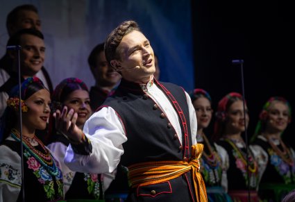 Zbliżenie na solistę chóru podczas koncertu z widocznych chórem w tle