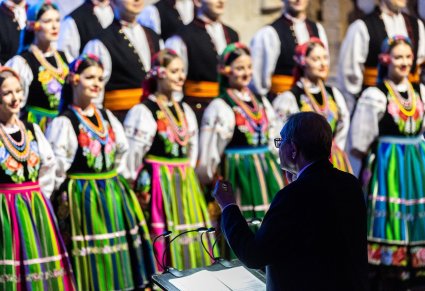 Na pierwszym planie zwrócony do chóru Mirosław Ziomek a przed nim chór w kostiumach łowickich