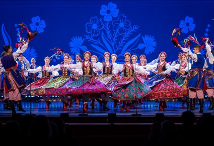 Tancerki w kostiumach krakowskich podczas obrotów na scenie, tancerze w kostiumach krakowskich stojący po bokach