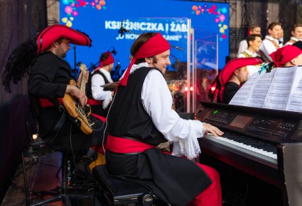 Zbliżenie na Akompaniatora w kostiumie pirackim w trakcie grania na instrumencie, w tle Gitarzysta i Perkusista