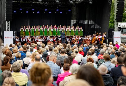 Na pierwszym planie publiczność na scenie Artyści w kostiumach kurpiowskich, widoczna orkiestra z Dyrygentem