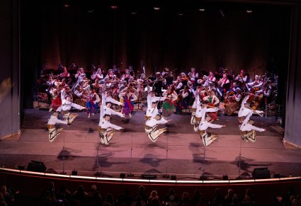 Na scenie Artyści Baletu w kostiumach podhalańskich podczas wykonywania choreografii tanecznej, w tle widoczna Orkiestra
