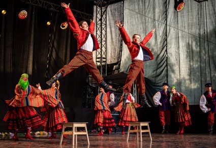 Na pierwszym planie dwóch Artystów w kostiumach sieradzkich wykonujący spektakularne akrobacje taneczne na scenie