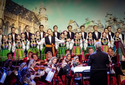 Dyrektor Jacek Boniecki zwrócony w stronę Orkiestry, za Orkiestrą Solista i Artyści chóru w kostiumach łowickich