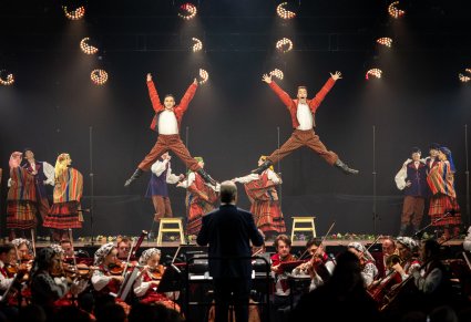 Na środku sceny Artyści w kostiumach sieradzkich w trakcie wykonywania choreografii tanecznej, widoczna również Orkiestra w kostiumach wilanowskich