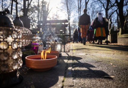 Na pierwszym planie palące się dwa znicze a w tle para Artystów w kostiumach kocierzewskich