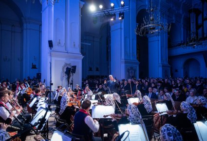 Na pierwszym planie dyrygujący Dyrektor zespołu "Mazowsze", przed nim orkiestra w kostiumach wilanowskich, widoczna publiczność koncertu kolęd i pastorałek