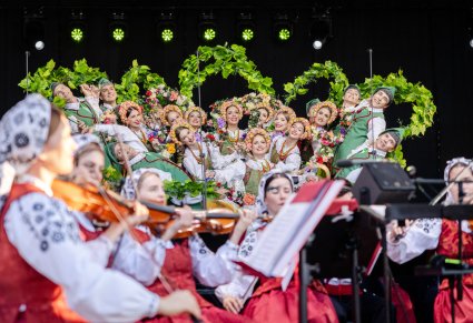 Widok przez Artystów Orkiestry w kostiumach wilanowskich na scenę na której Artyści w kostiumach lubuskich wykonują finałowy moment choreografii tanecznej