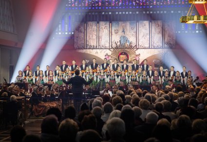 Przed Ołtarzem Artyści Chóru w kostiumach łowickich w trakcie śpiewu, Artyści Orkiestry w kostiumach wilanowskich oraz Dyrygent. Widoczna również część Orkiestry