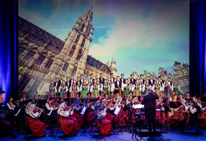 Dyrektor Jacek Boniecki zwrócony w stronę orkiestry, za nią Artyści z chóru w kostiumach łowickich ustawieni w rzędzie