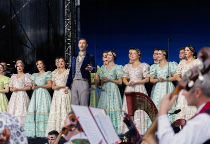 Na pierwszym planie Solista a za nim Artyści Chóru w kostiumach stylowych z końca XIX wieku, widoczna część Orkiestry w kostiumach wilanowskich