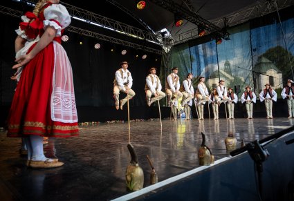 Artyści na scenie w kostiumach jurgowskich, na środku sceny mężczyźni wykonujący choreografię taneczną z drewnianymi kijkami