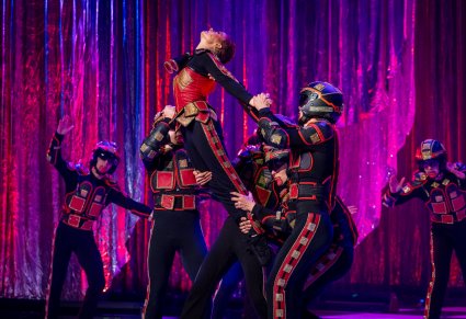 Scena postaci kwadratów. Postać kobieca wykonuje akrobacje, reszta postaci ją przytrzymuje