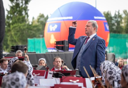 Kadr na Dyrygenta trzymającego w górze batutę, widoczna część Orkiestry w kostiumach wilanowskich