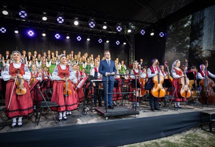 Na pierwszym planie Dyrygent wraz z orkiestrą w kostiumach wilanowskich, w tle chór w kostiumach łowickich.
