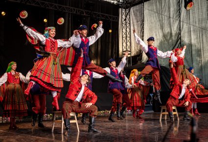 Grupa Artystów na scenie w kostiumach sieradzkich wykonująca spektakularne akrobacje taneczne