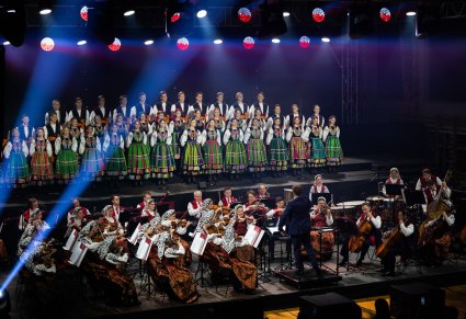 Na scenie Artyści Chóru w kostiumach łowickich, niżej Artyści Orkiestry w kostiumach wilanowskich wraz z Dyrektorem