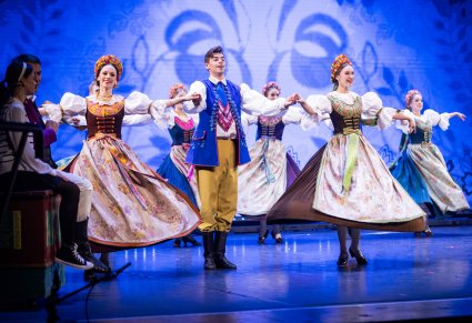 Artyści w kostiumie opolskim w trakcie wykonywania choreografii tanecznej w rogu sceny Pan Kajetan z Agnieszką siedzący na ręcznie malowanej skrzyni