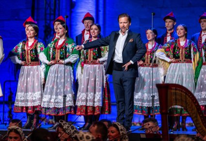 Na pierwszym planie solista w eleganckim garniturze a za nim Artyści z chóru w kostiumach krakowskich