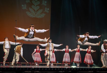 Na scenie Artyści w kostiumach jurgowskich podczas wykonywania choreografii tanecznej, Dwóch solistów wykonuje szpagaty w górze