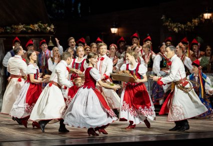 Zbliżenie na grupę Artystów wykonujących choreografię taneczną, trzymających w rękach tacę z potrawami