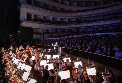 Na pierwszym planie orkiestra w kostiumach wilanowskich wraz z Dyrektorem, dyrygentem, w tle publiczność Teatru Wielkiego