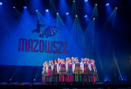 Na scenie Artyści w kostiumach opoczyńskich, za nimi wielki napisz MAZOWSZE wraz z logo zespołu