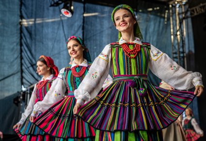 Trzy uśmiechnięte Artystki na scenie w kostiumach opoczyńskich