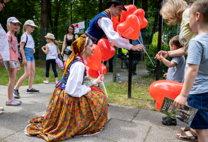 Artysci PZLPiT "Mazowsze" ubrani w kostiumach wręczają dzieciom balony w kształcie serca