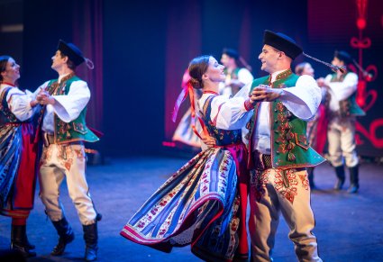 Na pierwszym planie para Artystów w kostiumach spiskich podczas wykonywania choreografii tanecznej na scenie