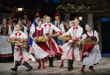 Zbliżenie na grupę Artystów w kostiumach stylizowanych. Artyści trzymają w rękach tacę z potrawami