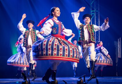 Zbliżenie na tancerkę w kostiumie spiskim w obrocie, w tle widoczni tancerze