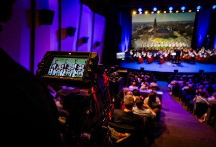 Na pierwszym planie monitor kamery, która jest skierowana w stronę sceny z Artystami. Na zdjęciu również widoczna jest publiczność