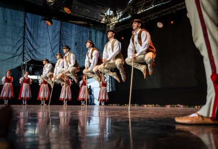 Na pierwszym planie Artyści w kostiumach jurgowskich  tańczący układ z kijkami po bokach sceny reszta część Artystów